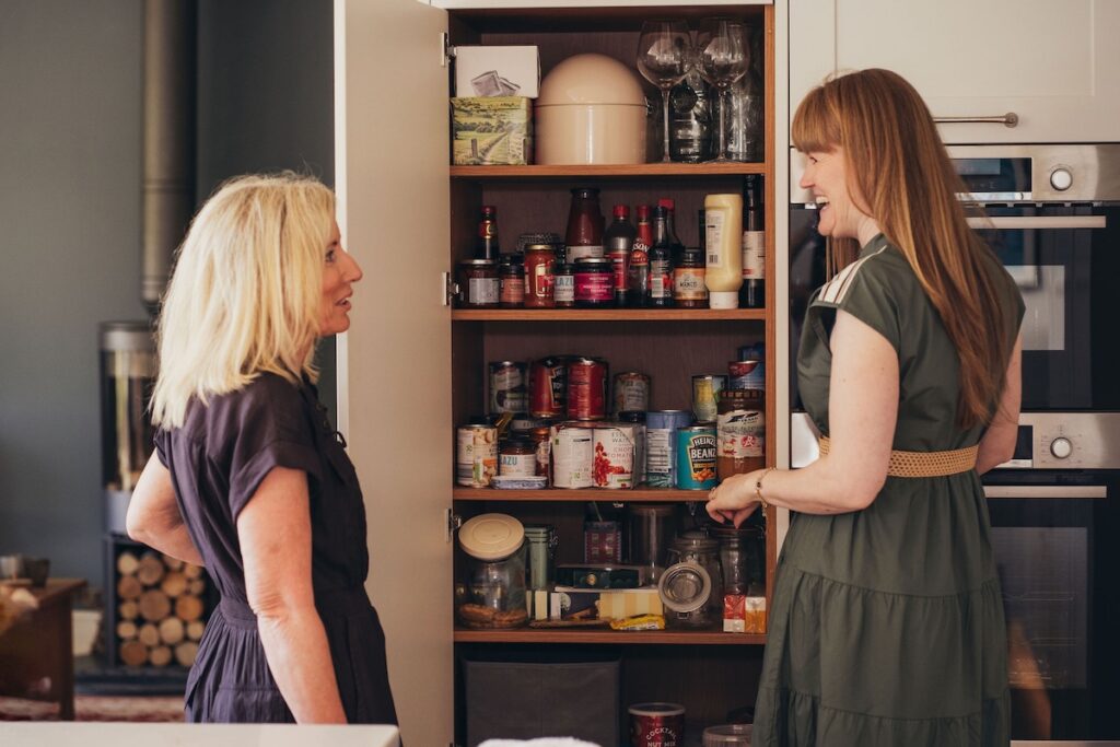 Kath chatting warmly with a client beside an open kitchen pantry during a consultation