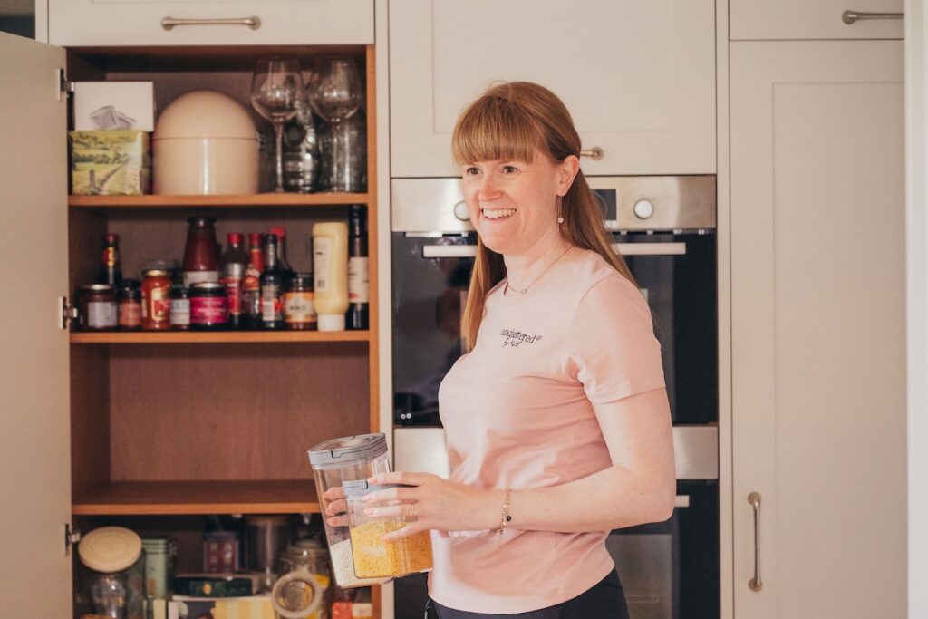 Professional Home Organiser Kath organising a kitchen pantry cupboard, holding storage containers and smiling