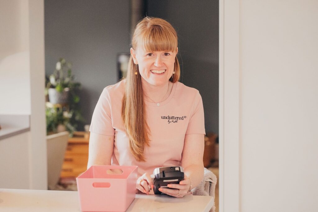 About Kath, professional organiser at Uncluttered by Kath, smiling with a storage box and label maker
